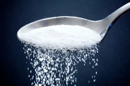 Sugar falling off a spoon on dark blue background