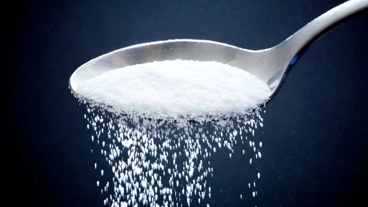 Sugar falling off a spoon on dark blue background